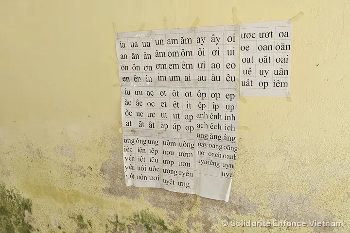 Những tờ bảng vần tiếng Việt dán trên bức tường vàng loang lổ nấm mốc.