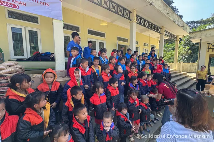 Children in new red and black coats gather on the school steps, under the operation’s banner.
