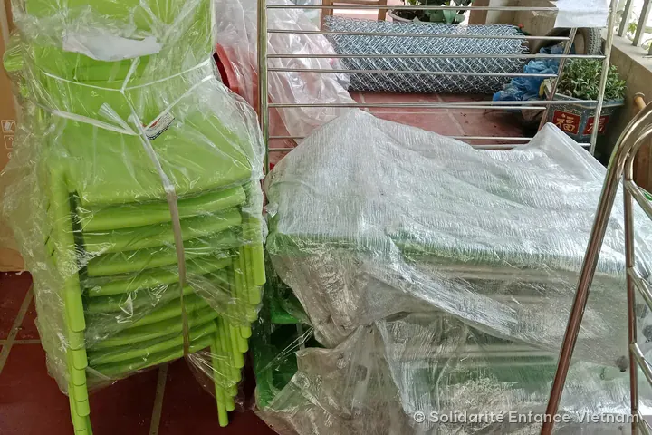 A stack of green children’s chairs in plastic film, next to a stainless steel towel rack and a roll of wire mesh.