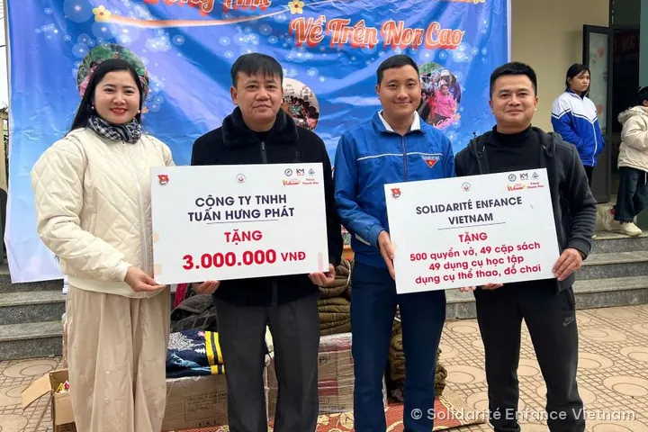 Bốn người đứng trước áp phích của chương trình, cầm hai tấm bảng: phần quà 3.000.000 VNĐ của một doanh nghiệp địa phương và phần quà của Solidarité Enfance Vietnam.
