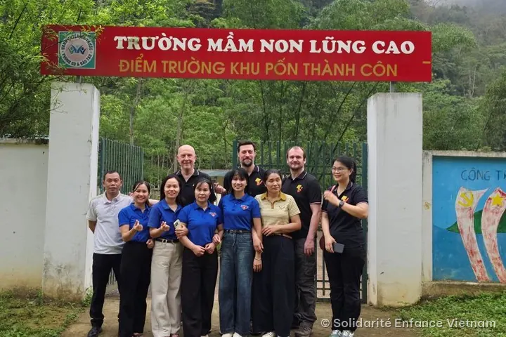 Mười một người chụp ảnh trước cổng trường, dưới tấm biển đỏ “Trường mầm non Lũng Cao – Điểm trường khu Pốn Thành Côn”.
