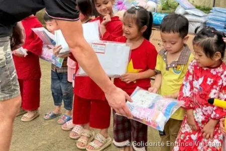 Một tình nguyện viên trao túi đồ dùng học tập cho một bé gái trong hàng các em nhỏ.