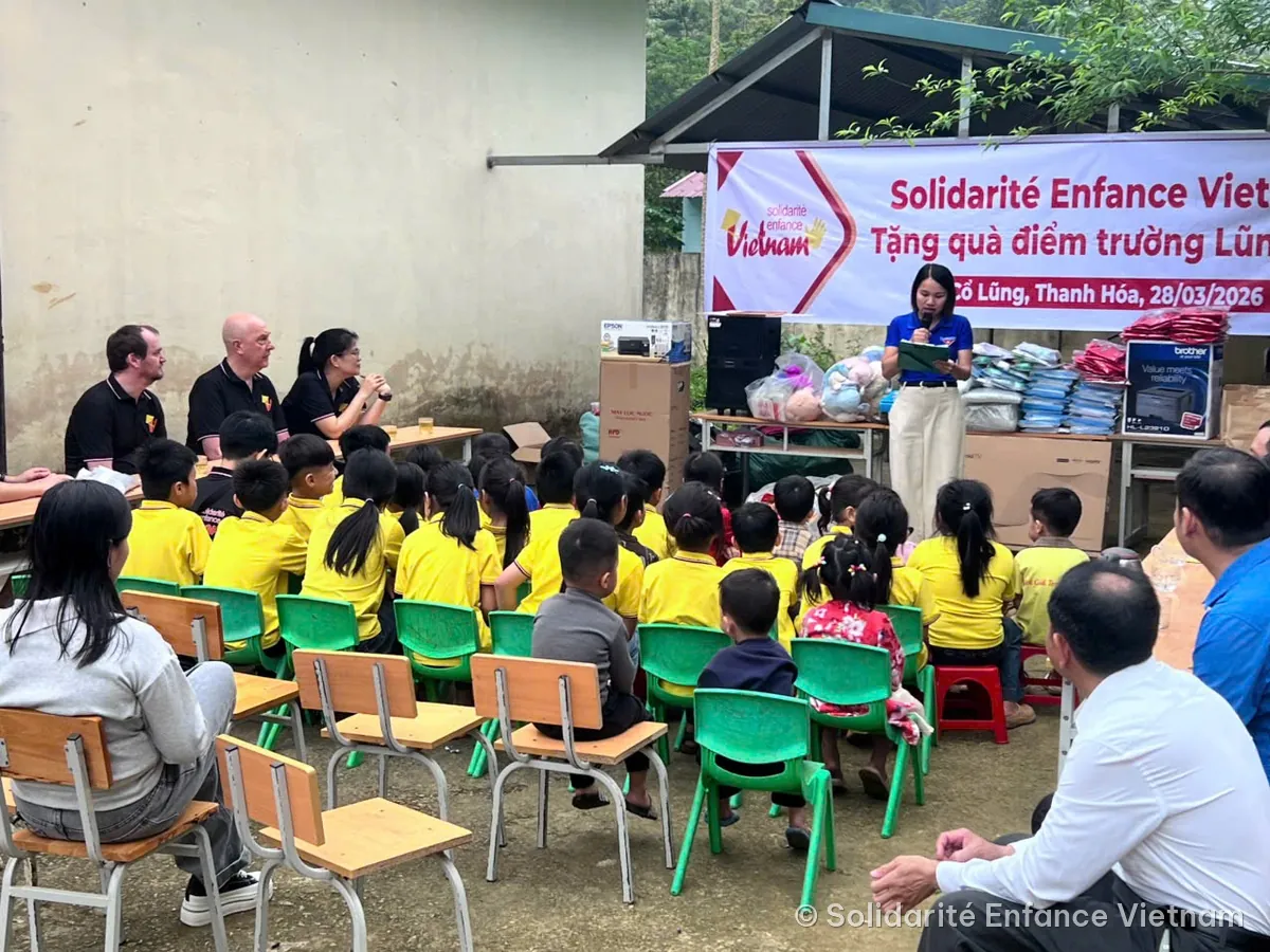 Gift handover at the Lũng Cao school: children in yellow polo shirts seated in front of the association’s banner.