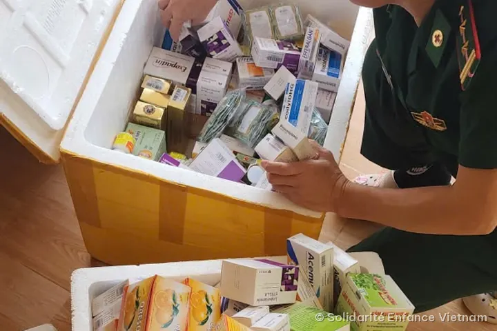 An officer in green uniform unpacks medicine boxes from two large polystyrene crates.