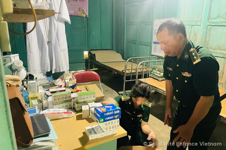 Two officers in green uniform arrange medicine boxes on a desk in the post’s medical room.