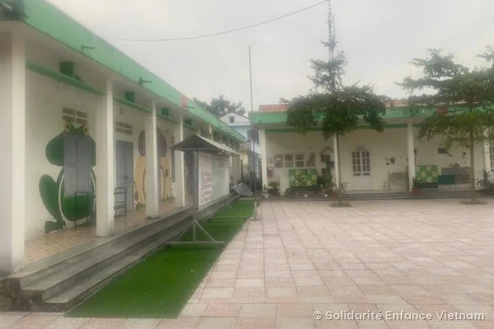 Tiled courtyard of the Tân Quang kindergarten, lined with white buildings with green roofs; a frog is painted on one wall.