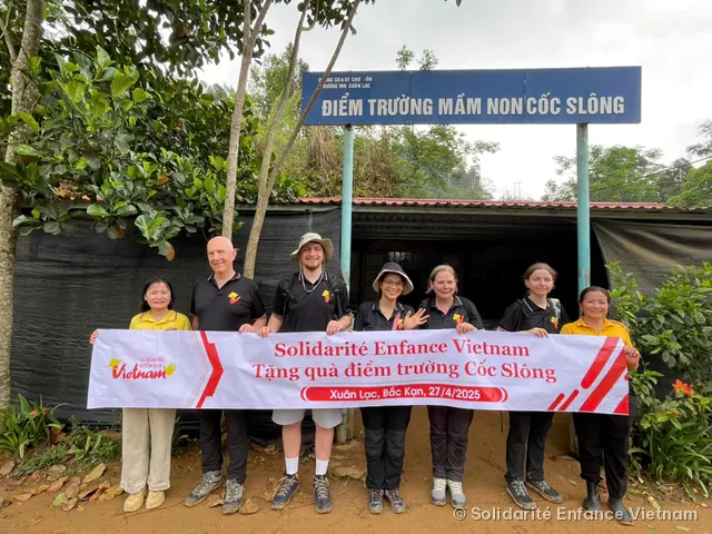 Sept personnes tiennent la banderole de l’association devant l’entrée de l’école maternelle de Cốc Slông.